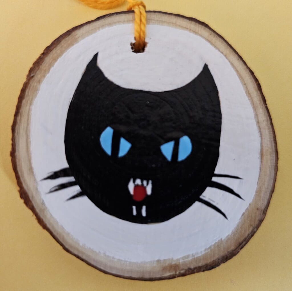 A black cat with blue eyes hanging on a tree branch.