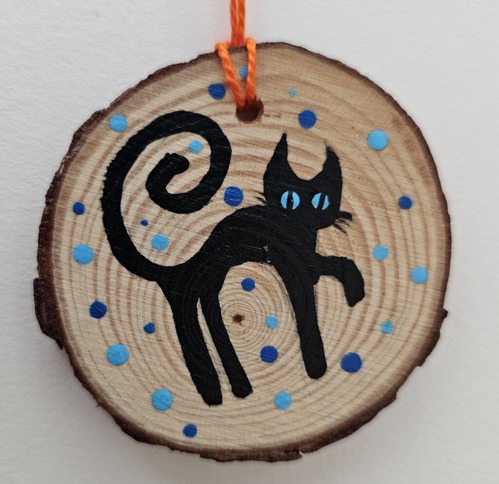 A black cat on a wooden slice with blue dots.