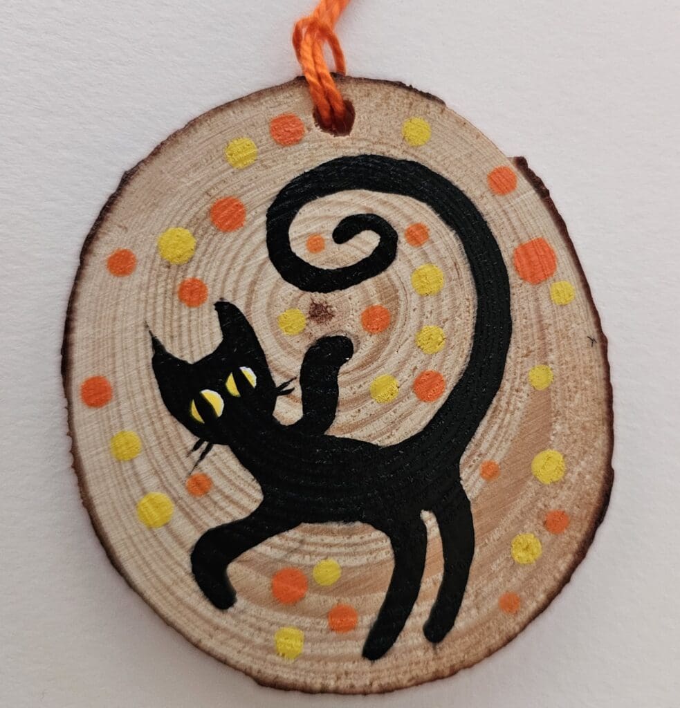 A black cat on a wooden slice with orange string.