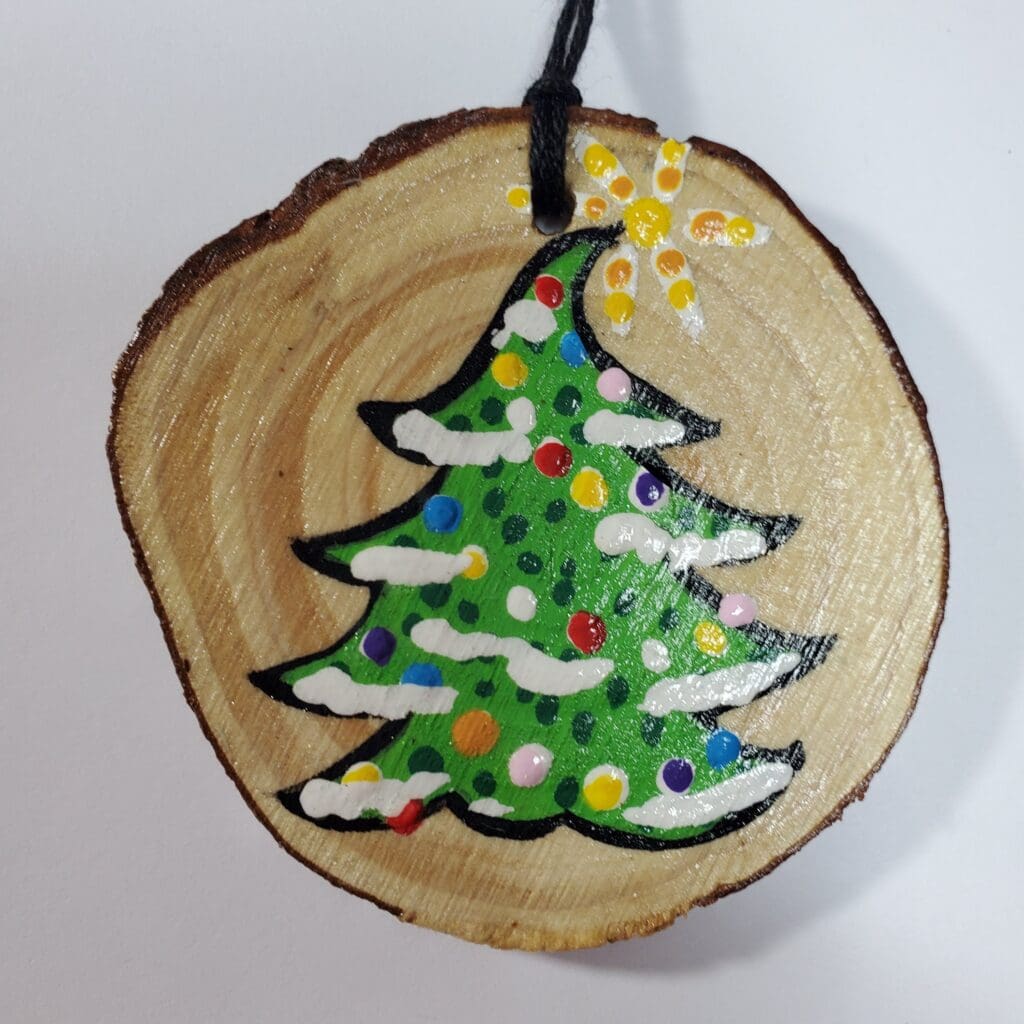 A wooden slice with a christmas tree painted on it.