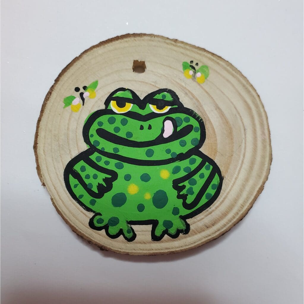 A wooden disc with a picture of a frog on it.