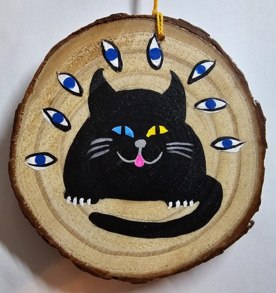 A black cat with blue eyes on a wood slice.