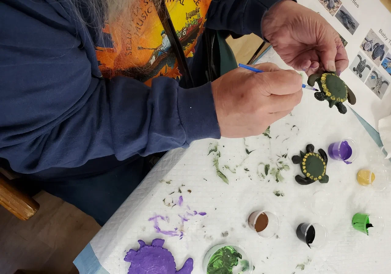 Person painting colorful turtle crafts on table.